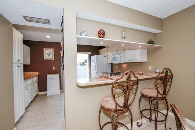 kitchen with visible vents, a kitchen bar, open shelves, white cabinetry, and white appliances