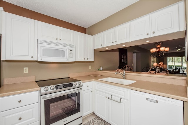 kitchen featuring light countertops, a notable chandelier, white cabinets, white appliances, and a sink