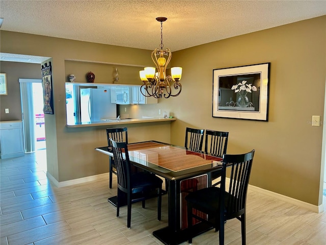 dining room featuring light wood-type flooring, baseboards, a notable chandelier, and a textured ceiling