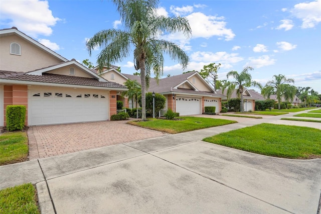 view of front of house with an attached garage, a tiled roof, decorative driveway, stucco siding, and a front lawn