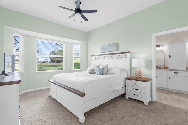 bedroom featuring a ceiling fan, light colored carpet, baseboards, and ensuite bathroom