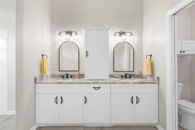 bathroom featuring double vanity, a sink, toilet, and baseboards