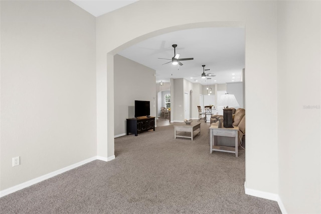 carpeted living area featuring arched walkways, a ceiling fan, and baseboards