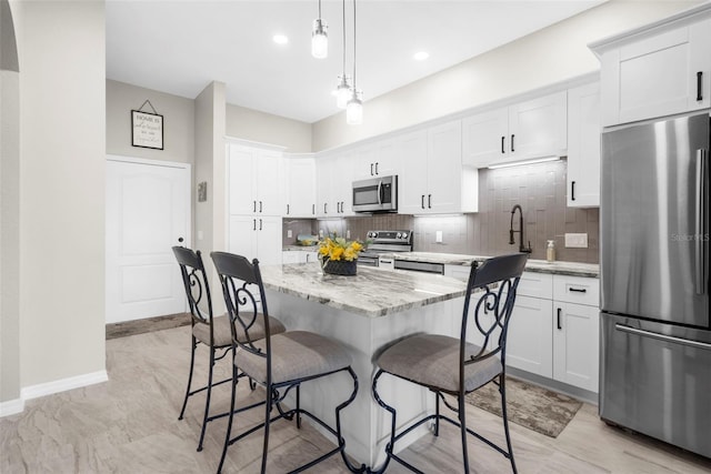 kitchen featuring light stone counters, stainless steel appliances, decorative backsplash, white cabinetry, and a kitchen breakfast bar