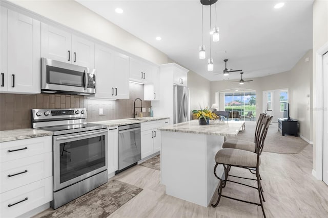 kitchen with a sink, white cabinets, appliances with stainless steel finishes, a center island, and tasteful backsplash