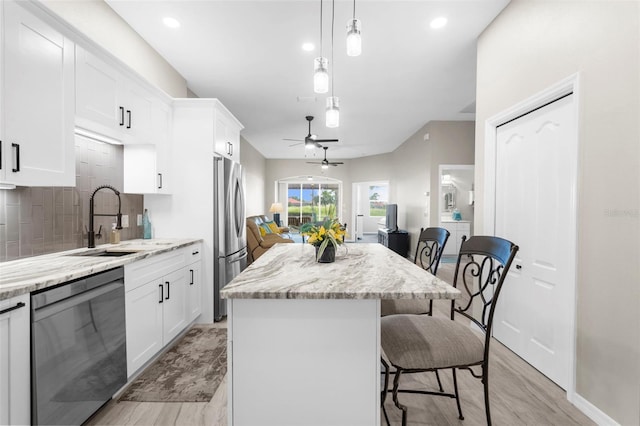 kitchen with stainless steel appliances, a breakfast bar, a kitchen island, a sink, and white cabinetry