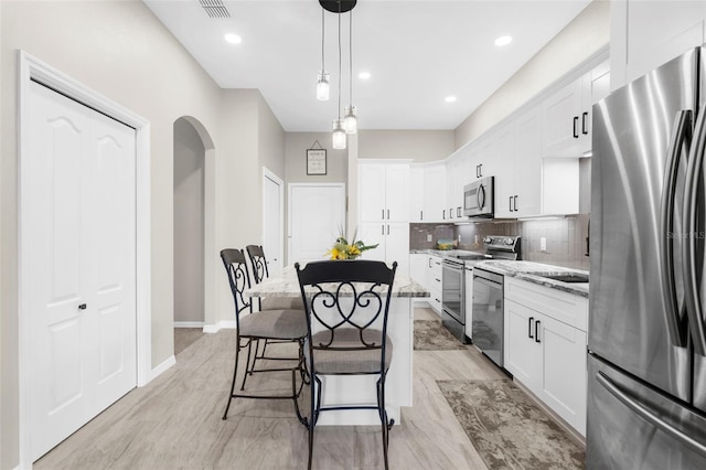 kitchen featuring white cabinets, appliances with stainless steel finishes, a kitchen breakfast bar, light stone countertops, and backsplash