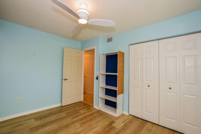 unfurnished bedroom featuring a textured ceiling, a closet, light hardwood / wood-style floors, and ceiling fan