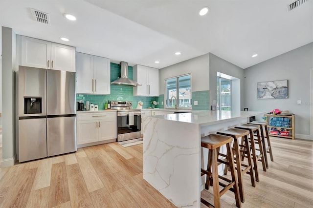 kitchen with light hardwood / wood-style floors, white cabinetry, stainless steel appliances, and wall chimney range hood