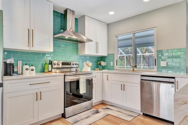 kitchen with backsplash, light hardwood / wood-style flooring, appliances with stainless steel finishes, white cabinetry, and wall chimney exhaust hood