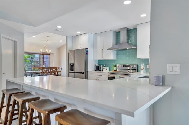 kitchen featuring stainless steel appliances, a notable chandelier, white cabinetry, wall chimney exhaust hood, and kitchen peninsula