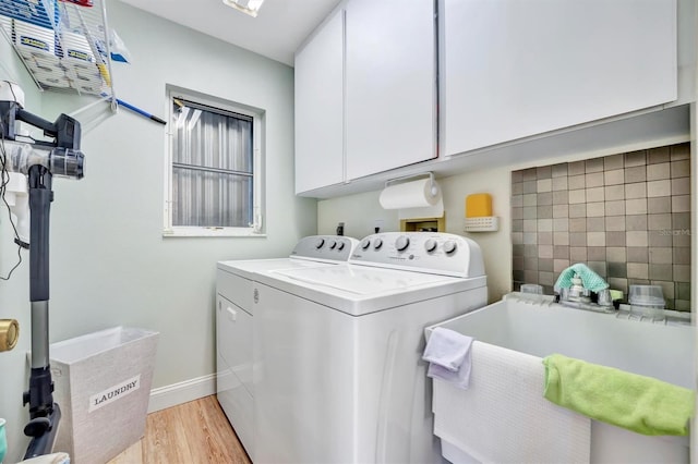 clothes washing area with washing machine and dryer, cabinets, sink, and light hardwood / wood-style flooring