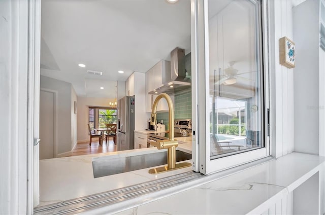 kitchen with backsplash, hardwood / wood-style floors, white cabinetry, wall chimney exhaust hood, and stainless steel fridge with ice dispenser