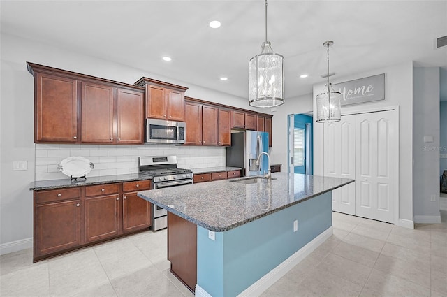 kitchen with sink, decorative light fixtures, dark stone counters, an island with sink, and stainless steel appliances