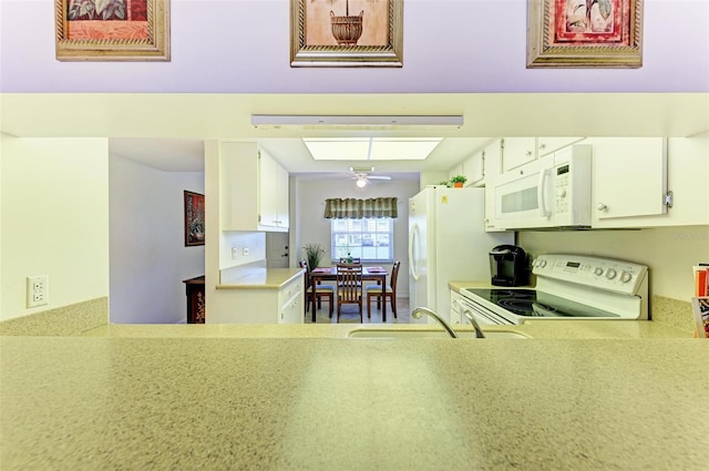 kitchen with white appliances, a skylight, sink, ceiling fan, and white cabinets