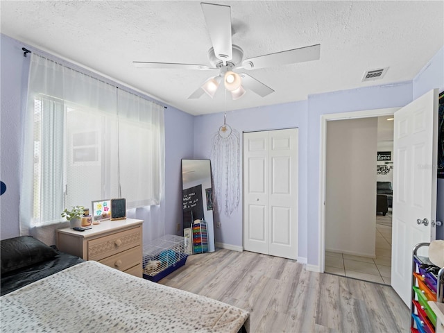 bedroom with a closet, light hardwood / wood-style floors, ceiling fan, and a textured ceiling