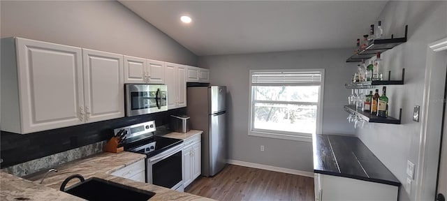 kitchen with hardwood / wood-style flooring, vaulted ceiling, stainless steel appliances, white cabinetry, and sink