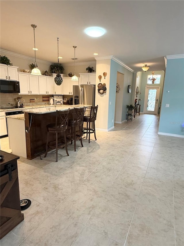 kitchen with a center island with sink, white cabinets, light stone countertops, decorative light fixtures, and a kitchen bar