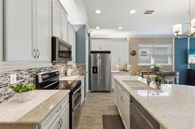 kitchen featuring pendant lighting, light stone counters, sink, white cabinetry, and stainless steel appliances