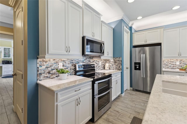 kitchen with light stone countertops, appliances with stainless steel finishes, crown molding, and white cabinetry