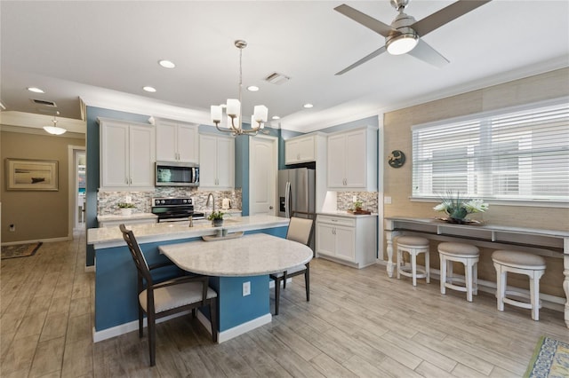 kitchen with appliances with stainless steel finishes, white cabinets, a breakfast bar, ceiling fan with notable chandelier, and decorative light fixtures