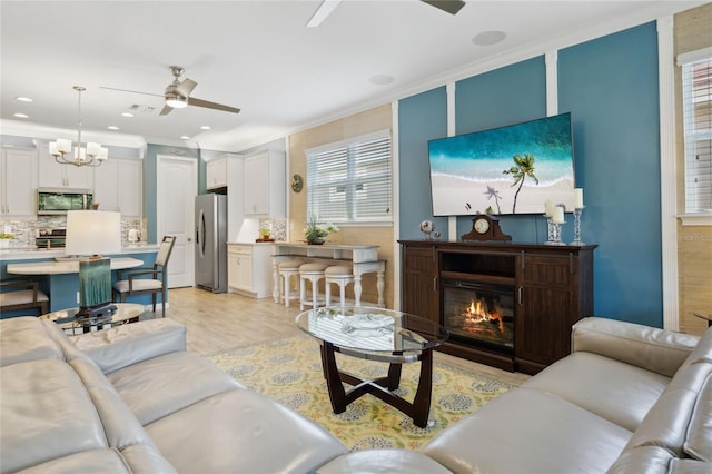 living area with ceiling fan with notable chandelier, visible vents, light wood finished floors, a glass covered fireplace, and crown molding