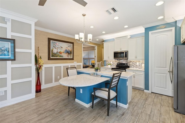 kitchen with white cabinetry, appliances with stainless steel finishes, a kitchen bar, a center island with sink, and pendant lighting