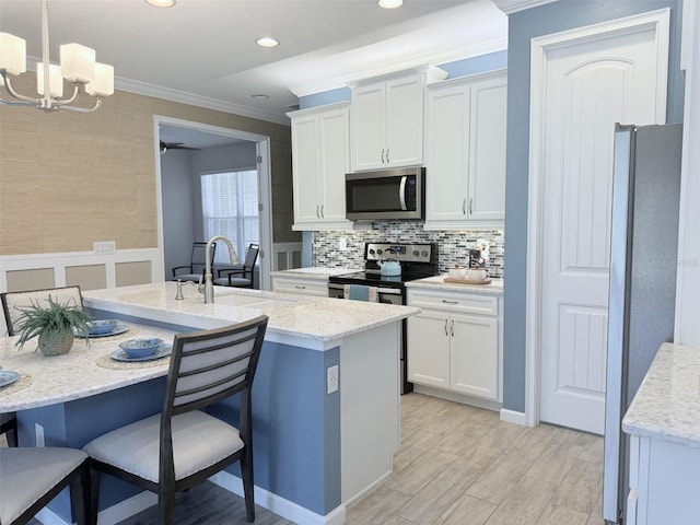 kitchen featuring an island with sink, appliances with stainless steel finishes, pendant lighting, and white cabinets