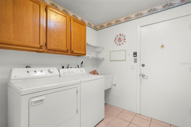 laundry area featuring light tile patterned floors, cabinets, washer and dryer, and a textured ceiling