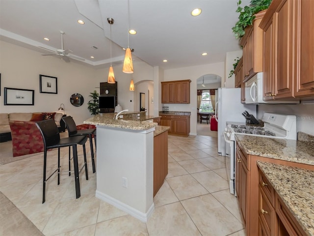 kitchen featuring ceiling fan, a center island with sink, light stone counters, and white appliances