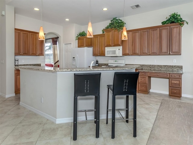 kitchen with an island with sink, white appliances, pendant lighting, and light stone countertops