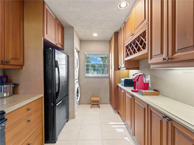 kitchen featuring black refrigerator, stacked washer / drying machine, and light tile patterned floors