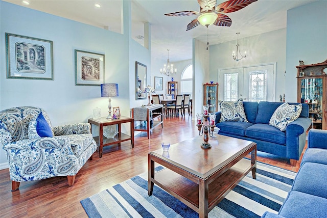 living room with ceiling fan with notable chandelier, a high ceiling, hardwood / wood-style flooring, and french doors