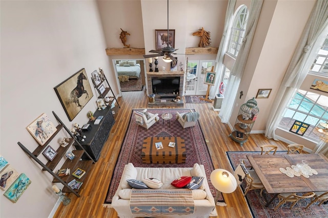 living room with a towering ceiling, ceiling fan, wood-type flooring, and plenty of natural light