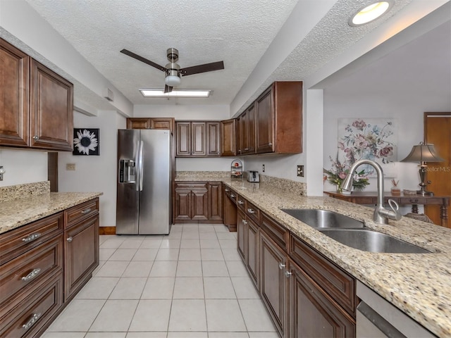 kitchen with light stone counters, light tile patterned floors, appliances with stainless steel finishes, a textured ceiling, and sink