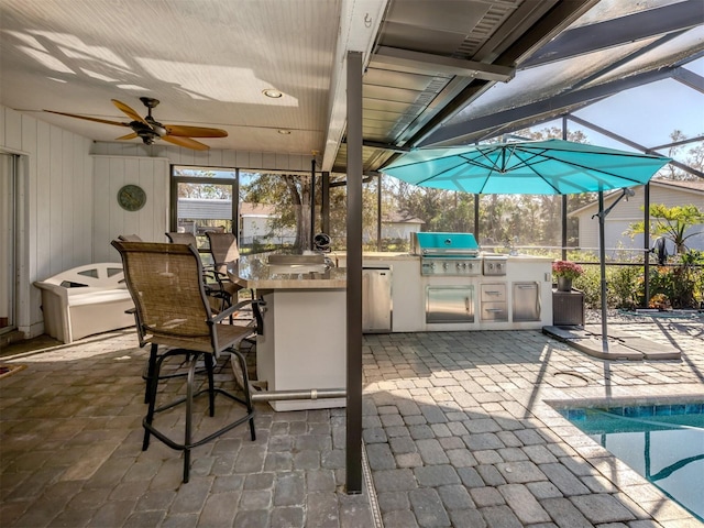 view of patio featuring exterior kitchen, ceiling fan, a grill, and a lanai