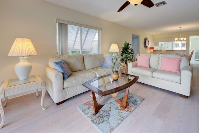 living room featuring light hardwood / wood-style flooring, ceiling fan with notable chandelier, and a healthy amount of sunlight