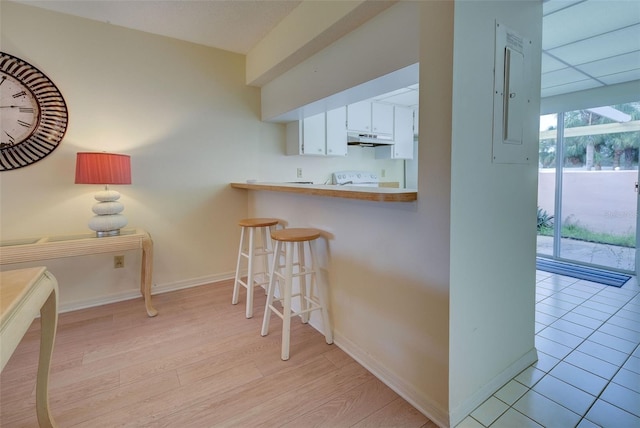 kitchen with a kitchen bar, light wood-type flooring, kitchen peninsula, and white cabinetry