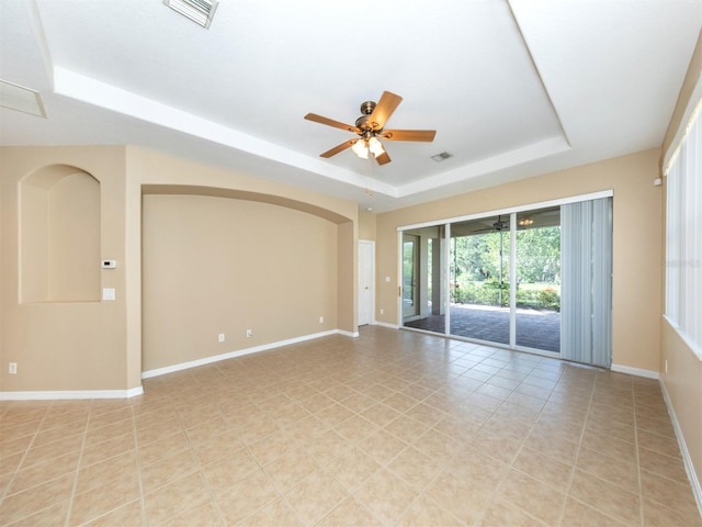 tiled empty room featuring ceiling fan and a raised ceiling