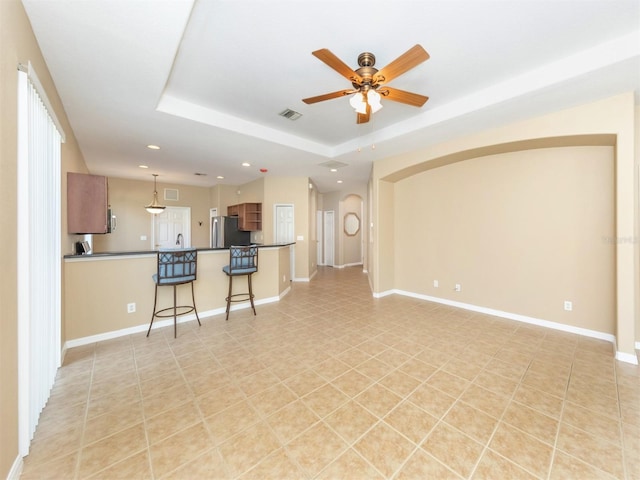 unfurnished living room featuring a raised ceiling, light tile patterned floors, and ceiling fan