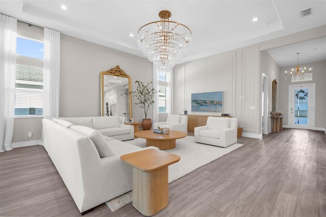 living room featuring light hardwood / wood-style floors, a raised ceiling, and an inviting chandelier