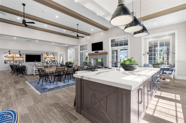 kitchen with ceiling fan, pendant lighting, beam ceiling, light hardwood / wood-style flooring, and a center island