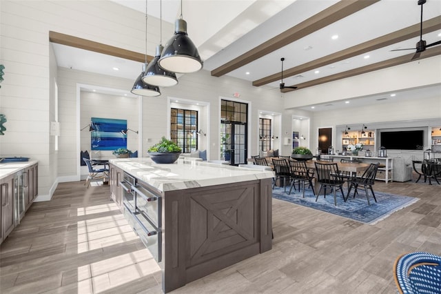 kitchen with beam ceiling, ceiling fan, light stone counters, pendant lighting, and a spacious island