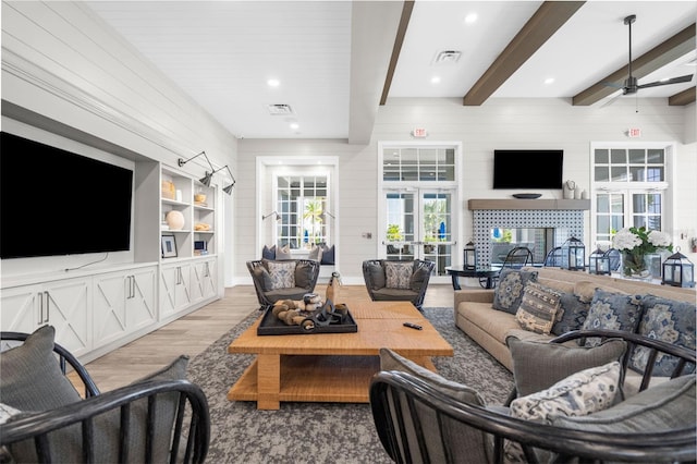 living room featuring a tile fireplace, french doors, light hardwood / wood-style flooring, ceiling fan, and beam ceiling