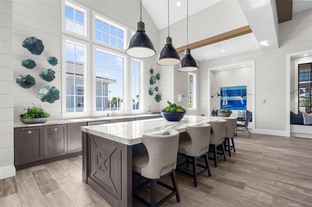 kitchen with wooden walls, light wood-type flooring, decorative light fixtures, a kitchen island, and light stone counters