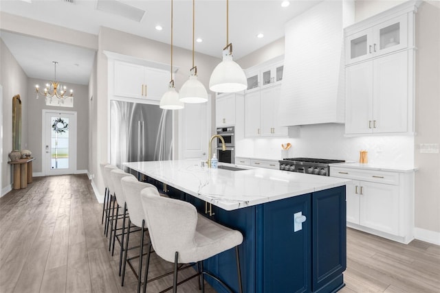 kitchen with white cabinetry, stainless steel appliances, pendant lighting, a kitchen island with sink, and light wood-type flooring