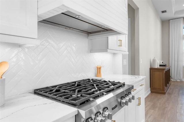 kitchen featuring light stone countertops, light hardwood / wood-style flooring, premium range hood, decorative backsplash, and white cabinets