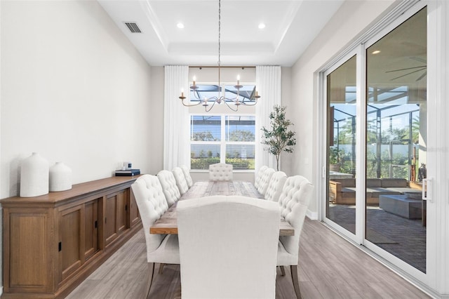 dining room featuring plenty of natural light, an inviting chandelier, light wood-type flooring, and a tray ceiling