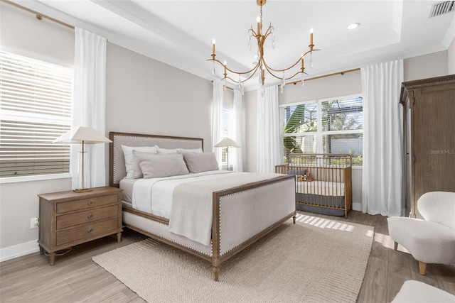 bedroom with a chandelier, a raised ceiling, light hardwood / wood-style flooring, and ornamental molding