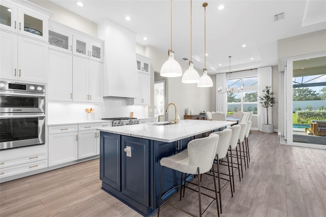 kitchen featuring pendant lighting, white cabinets, a kitchen island with sink, and light hardwood / wood-style flooring